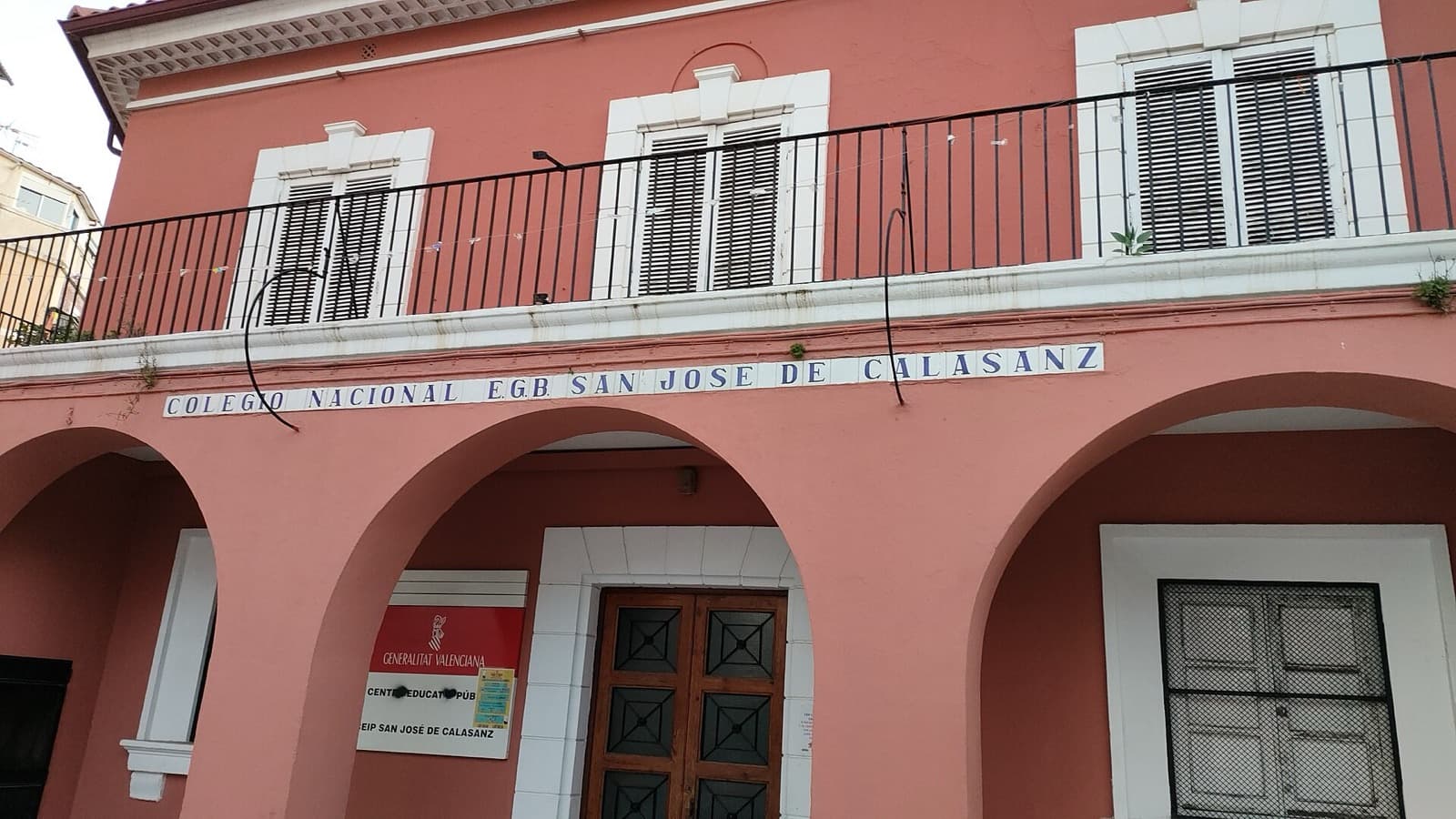 Façade rose à arcades de l’école publique CEIP San José de Calasanz à Valencia, avec le panneau de la Generalitat Valenciana