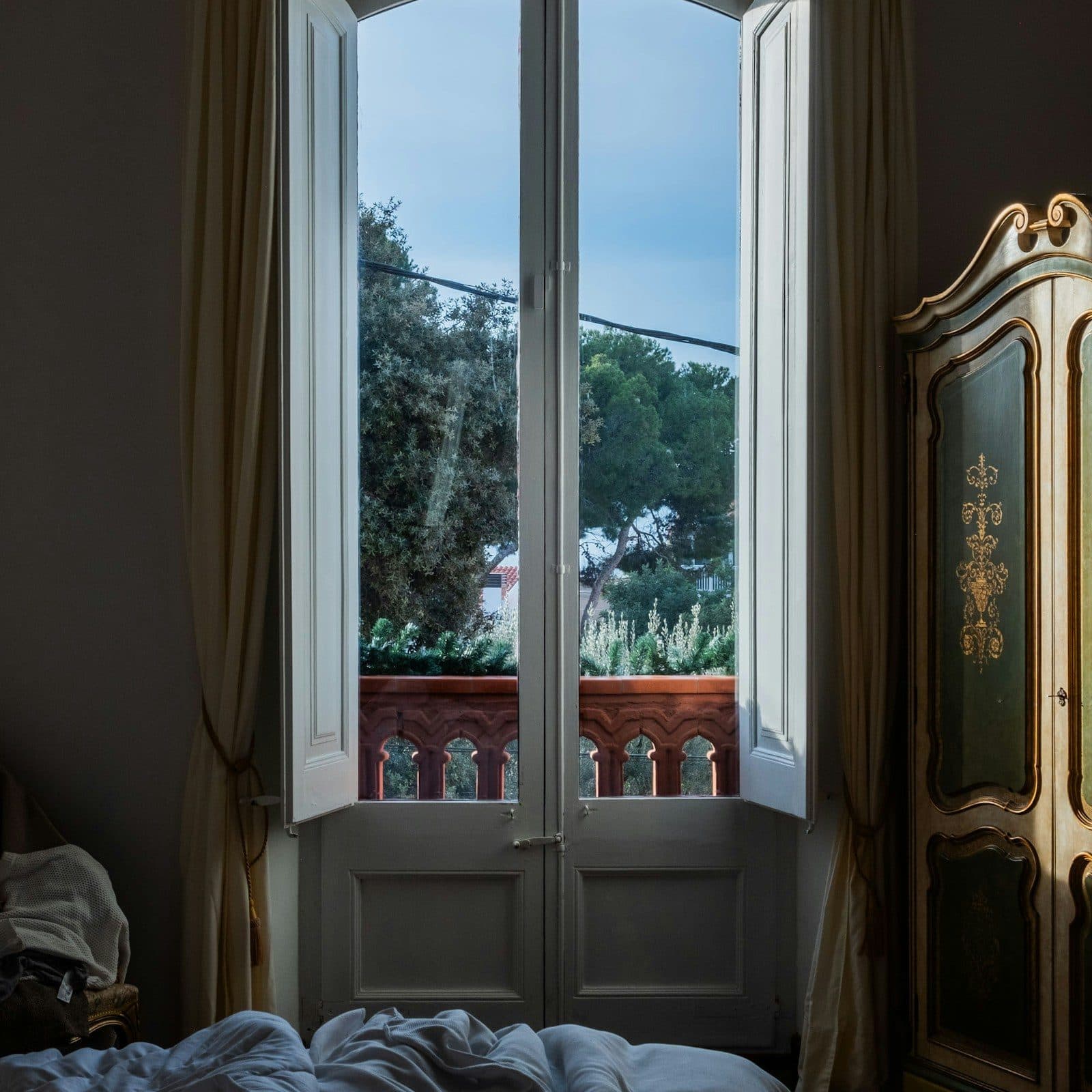 Chambre dans un appartement ancien : porte-fenêtre ouverte sur un balcon, carreaux de ciment au sol