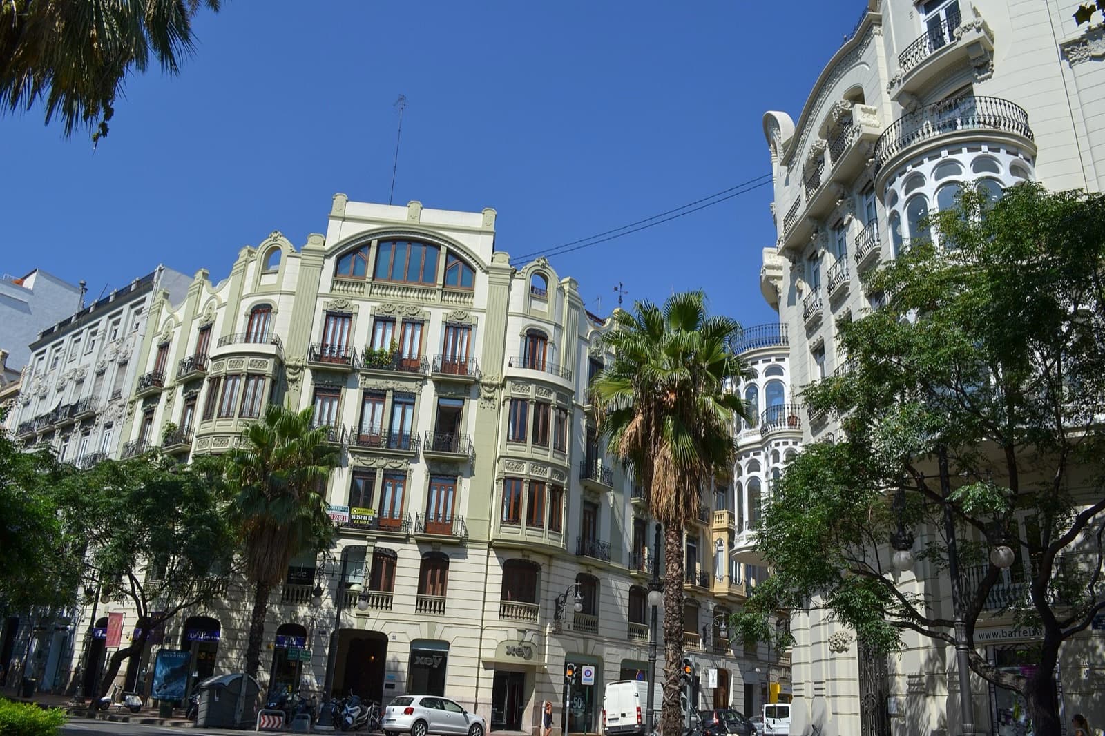 Immeubles anciens à balcons et miradors vitrés à l’angle de la Gran Via Marqués del Turia, palmiers au premier plan (Valencia)