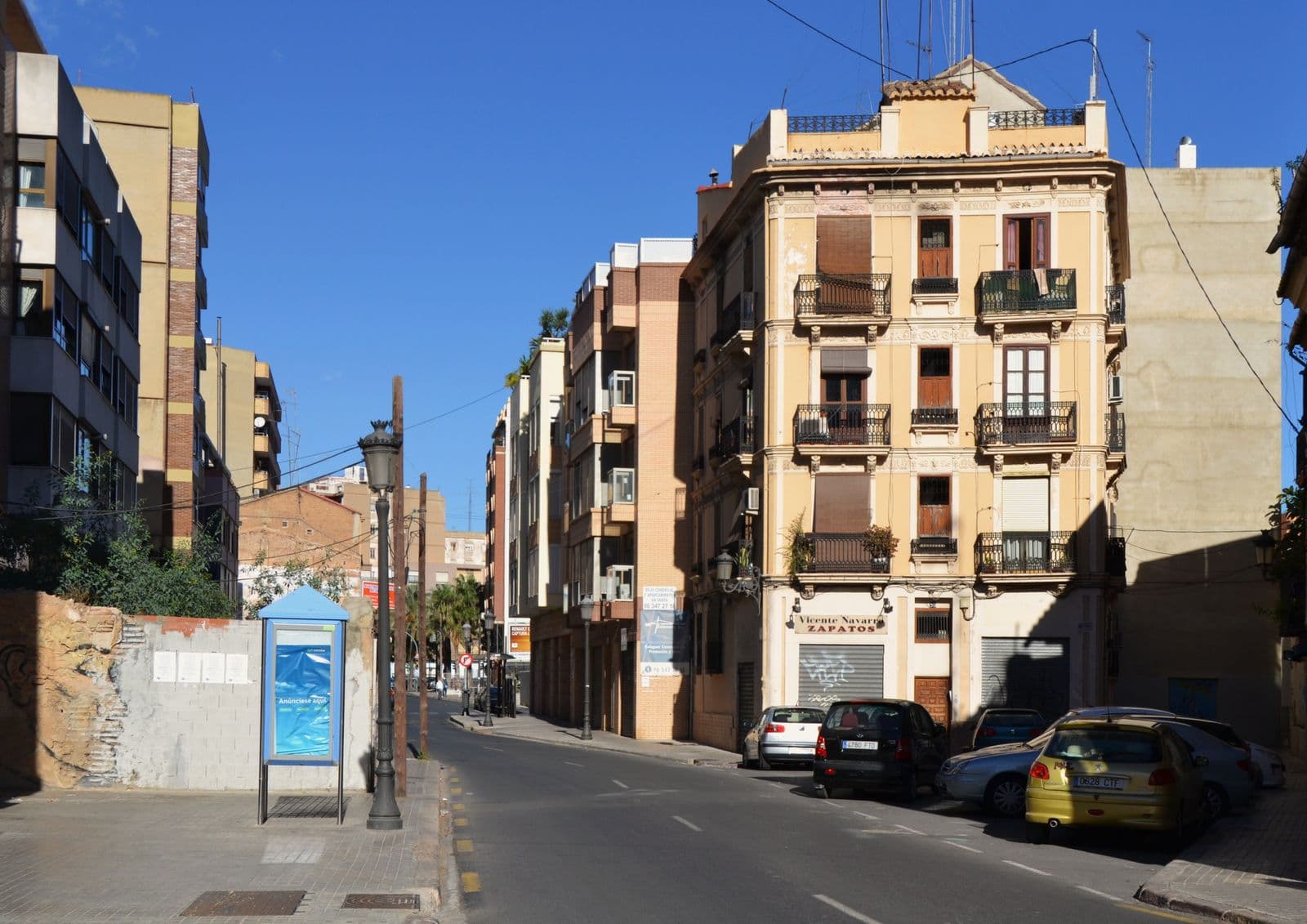 Le carrer de Sagunt à Morvedre (La Saïdia, Valencia) : immeuble ancien à balcons en fer forgé à l’angle, immeubles plus récents au fond, voitures garées