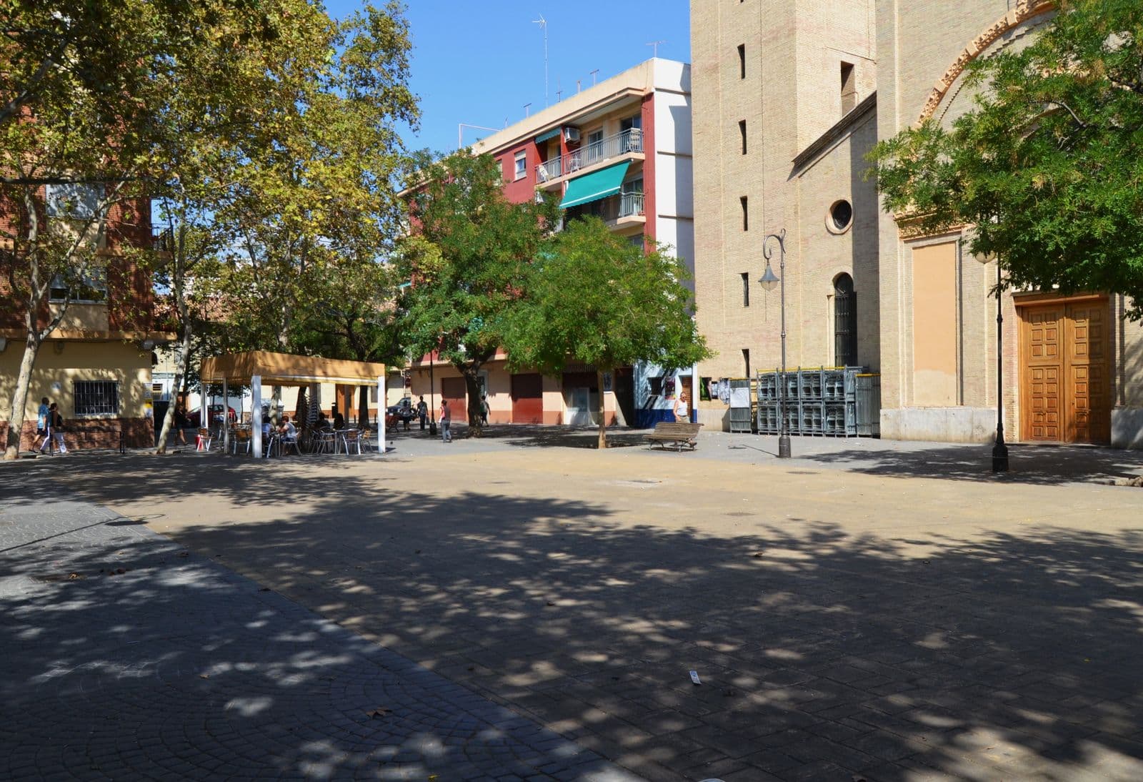 La plaça de l’Església de Benicalap : façade claire de l’église, terrasse sous les arbres et immeubles d’habitation (Valencia)