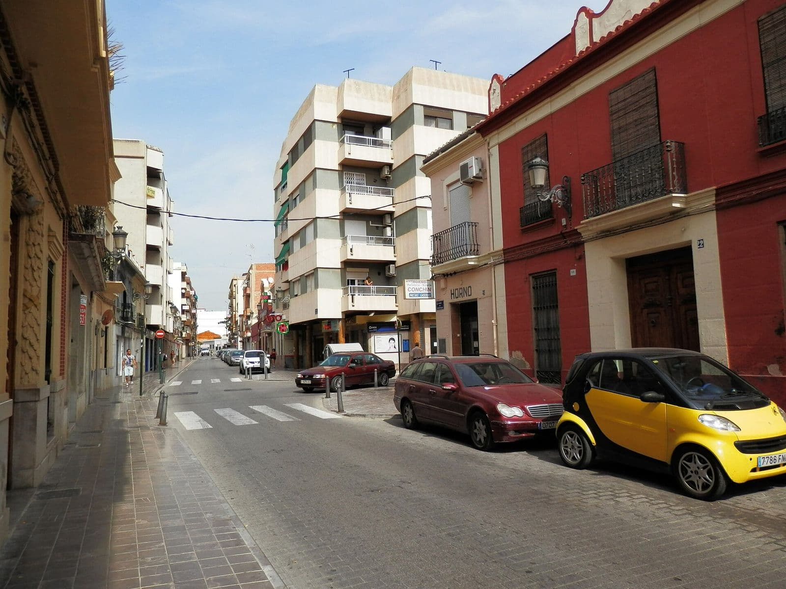 Le carrer de Felipe Valls à Benimàmet : maisons de village à balcons, dont une façade rouge, face à un immeuble d’habitation de cinq étages, voitures garées le long de la rue (Valencia)