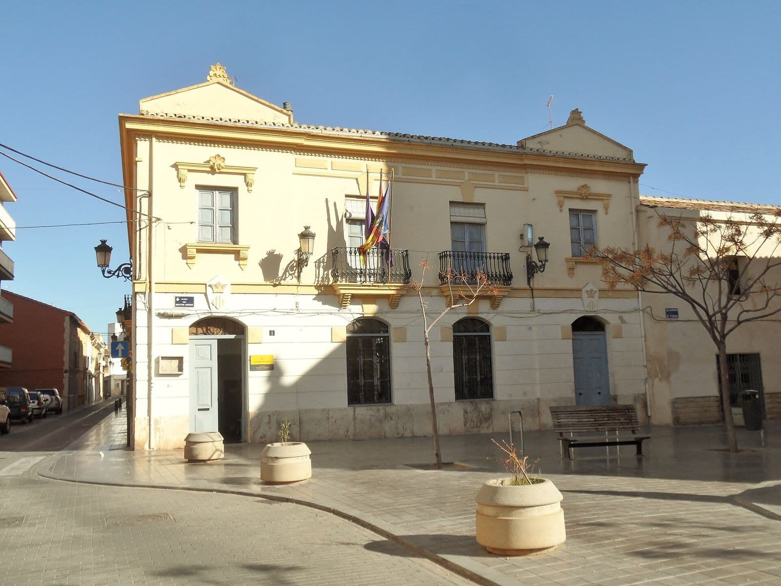 L’alcaldia de Benimàmet sur la plaça del Doctor Ximeno : maison de deux niveaux à façade crème, balcons en fer forgé et drapeaux, place piétonne pavée (Valencia)