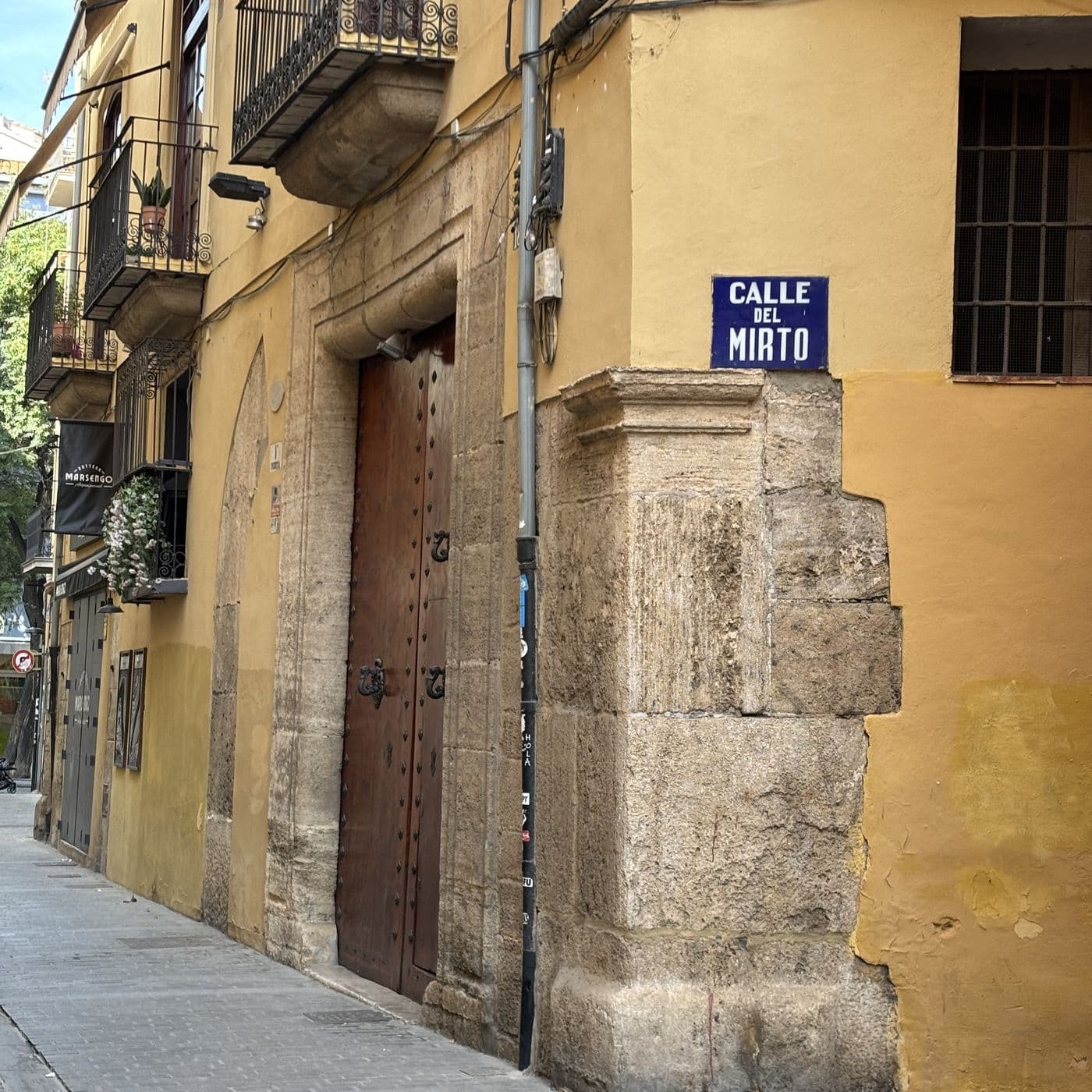 Angle d’un immeuble ancien de la calle del Mirto à El Carmen : pierre de taille, porte cochère en bois, balcons en fer forgé et plaque de rue bleue