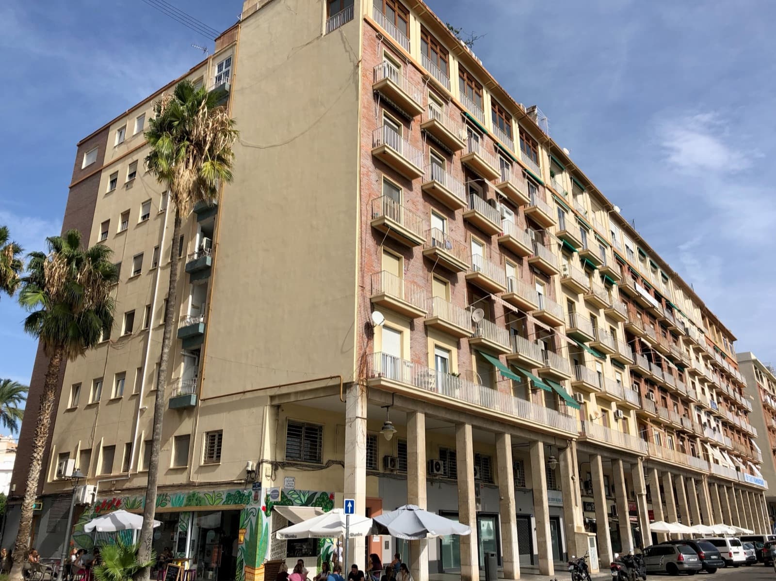 Immeuble d’habitation à balcons avec une galerie à arcades et des terrasses de café, à l’angle des rues Josep Aguirre et Doctor J.J. Dòmine (El Grau, Valencia)