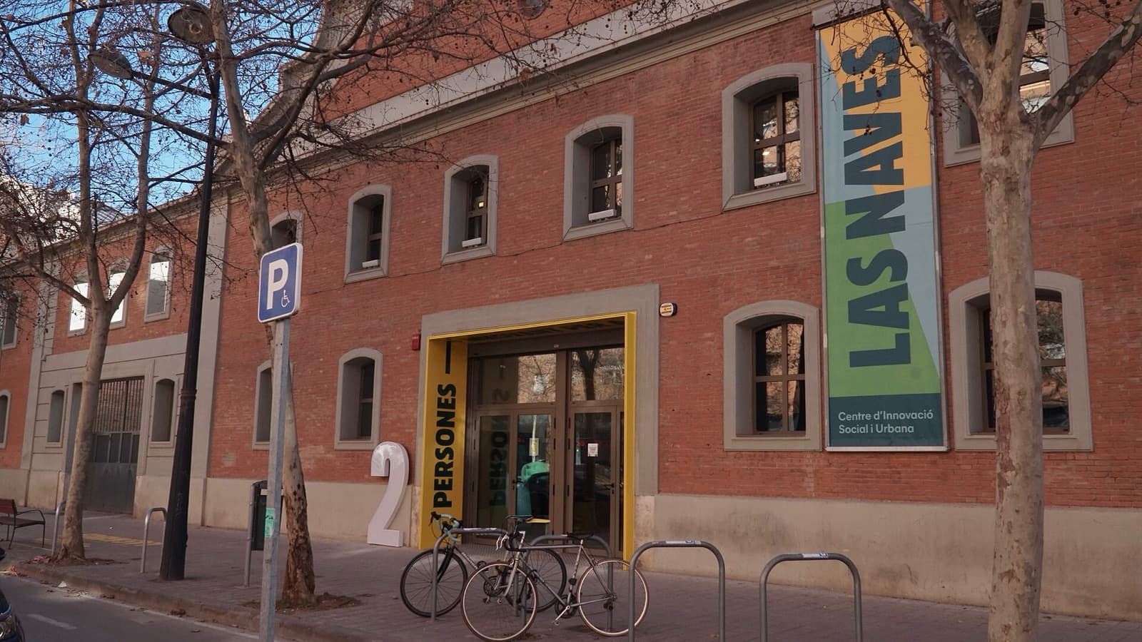 Façade en brique de Las Naves, le centre d’innovation sociale et urbaine de la ville de València, avec sa bannière et des vélos garés