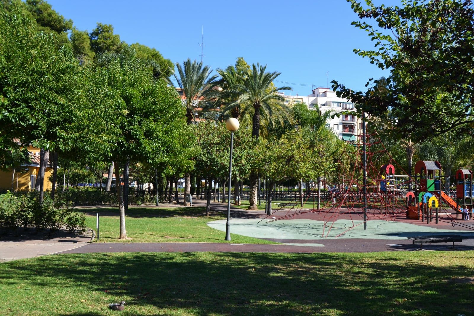 Le Parc de l’Oest à Valencia : pelouse, arbres, palmiers et aire de jeux pour enfants, immeubles du quartier en arrière-plan