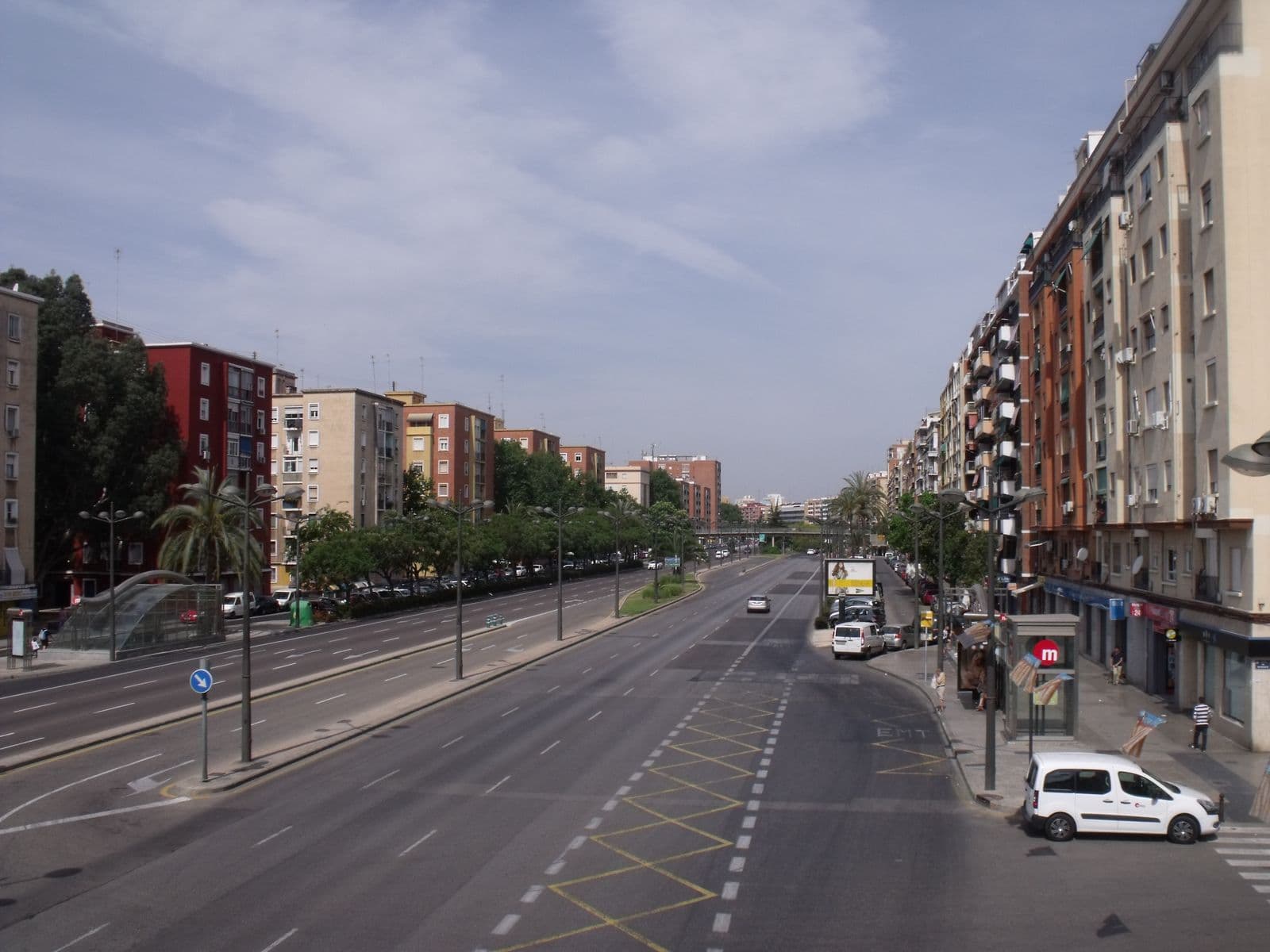 L’avenue del Cid à Valencia vue d’une passerelle : deux chaussées séparées par un terre-plein arboré, immeubles de logements des deux côtés, auvent vitré d’une entrée de métro à gauche et panneau du métro à droite