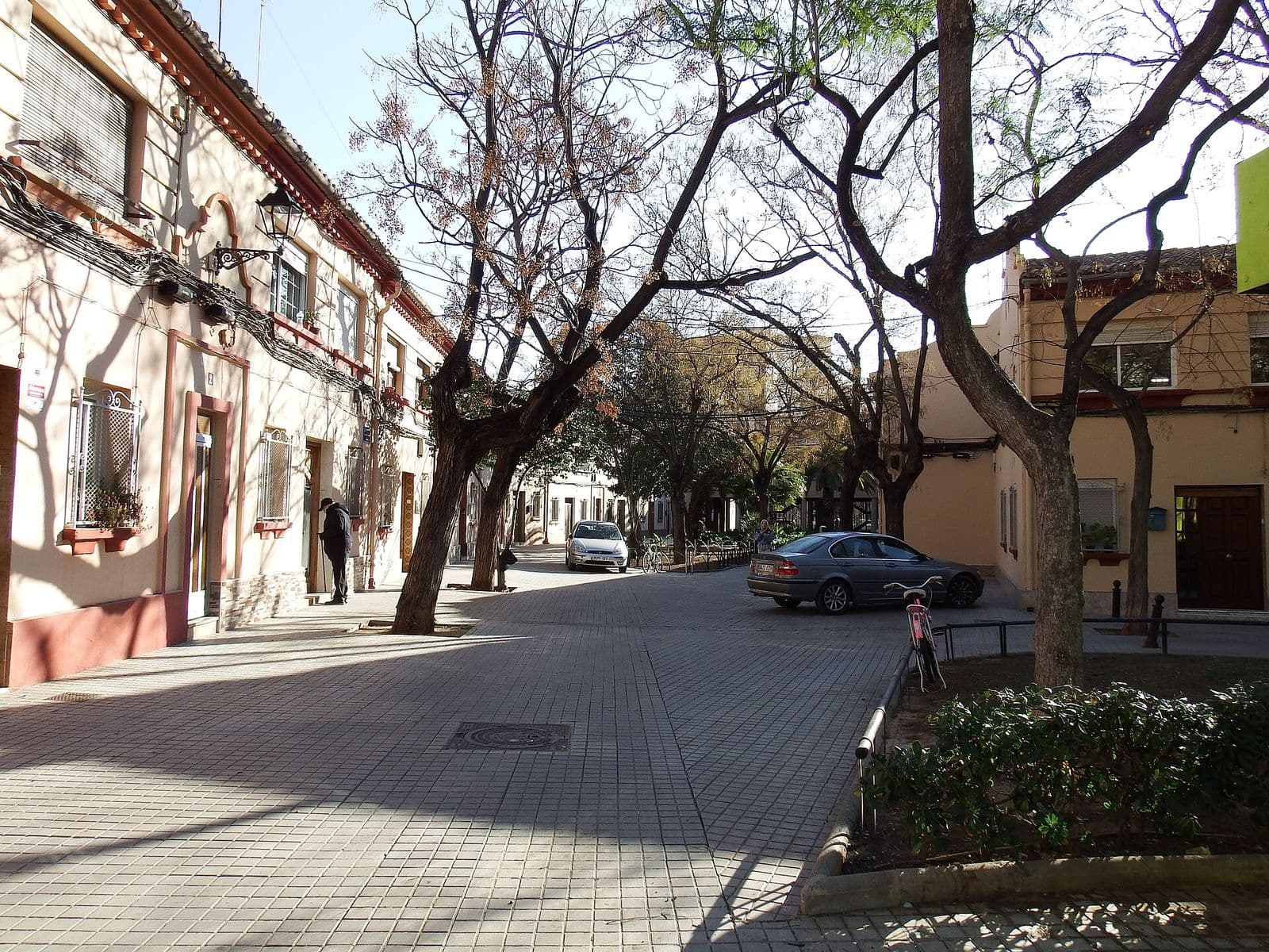 Rue pavée bordée d’arbres et de maisons basses à un étage, aux façades claires, à Torrefiel (Valencia)