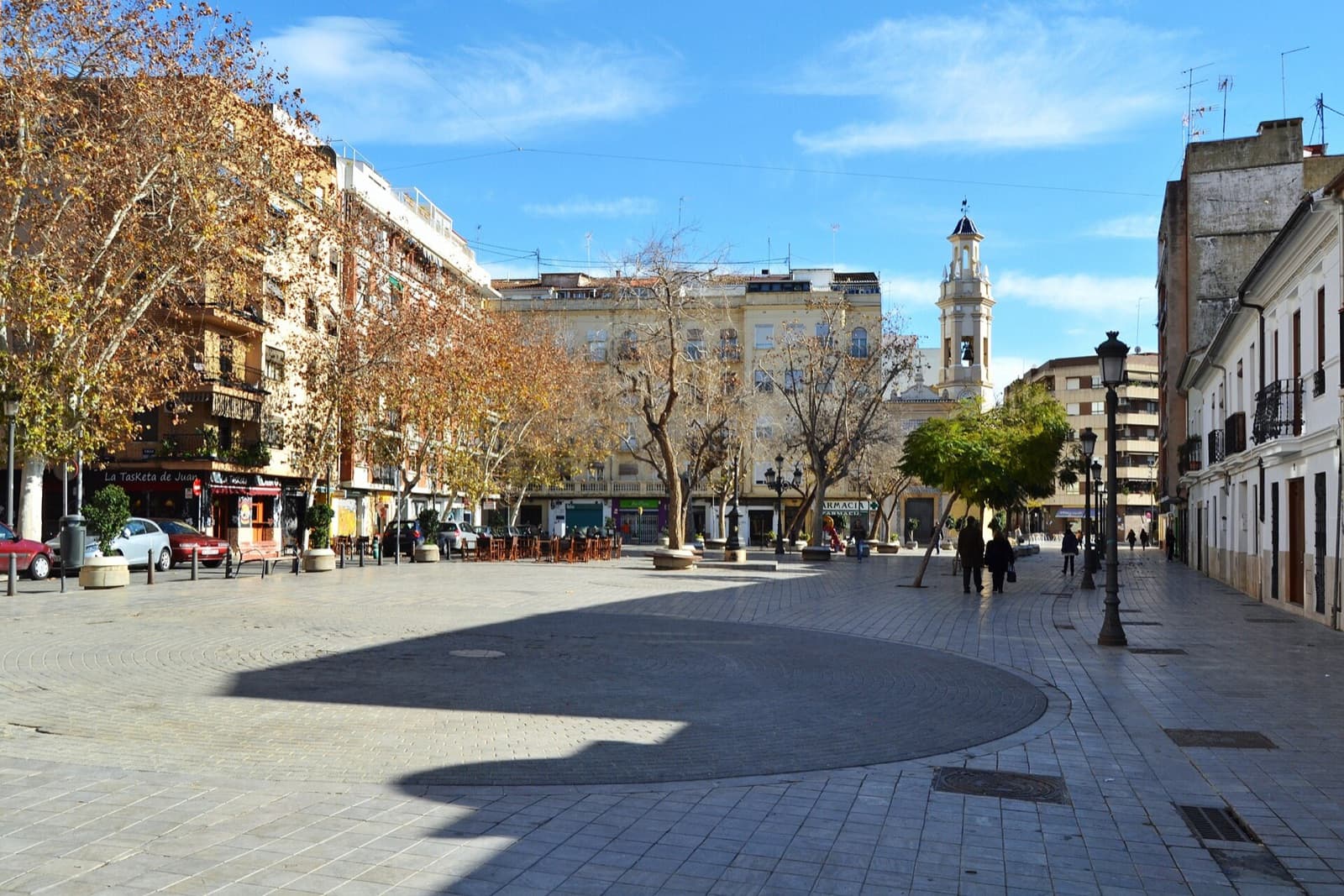 Place piétonne de Patraix à Valencia : arbres, terrasse de café, immeubles et clocher de l’église au fond