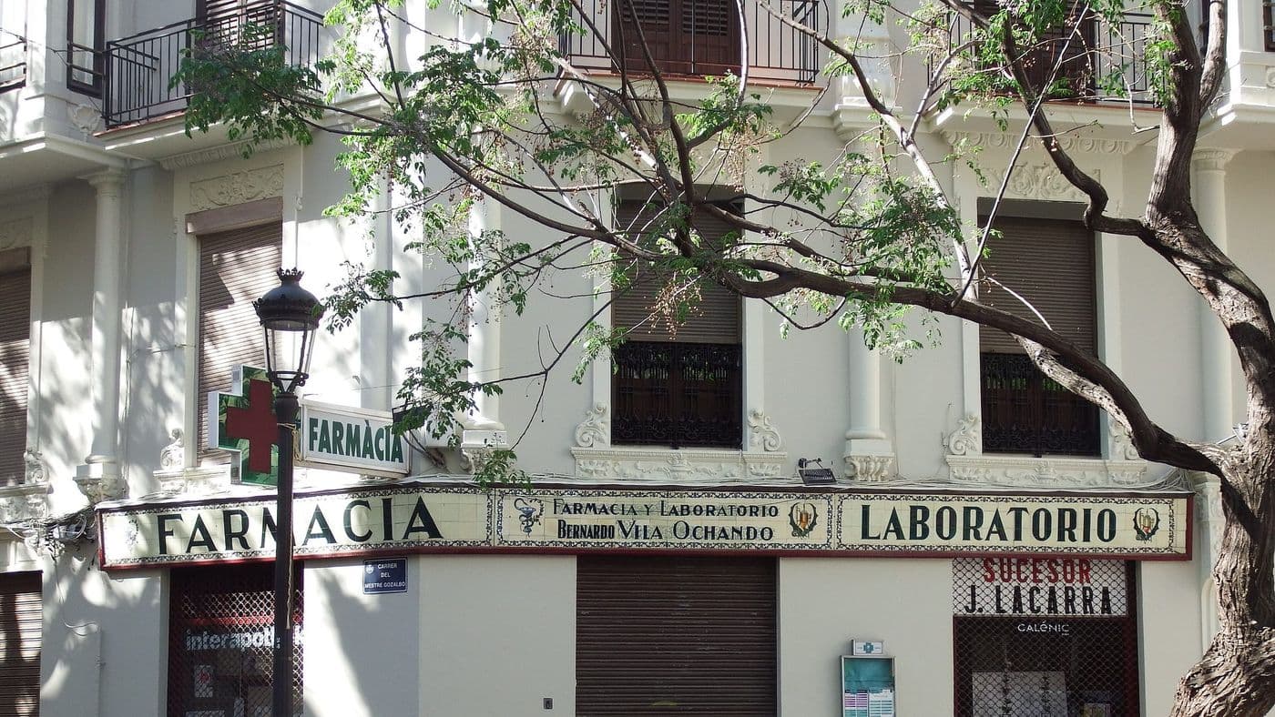 La croix d’une pharmacie et son ancienne enseigne en céramique « Farmacia y Laboratorio », au coin d’une rue de Valencia